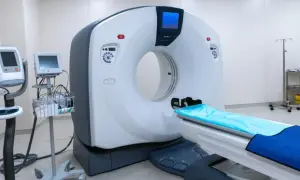 Nowoczesny aparat do tomografii komputerowej, gotowy do wykonania badania z kontrastem. Obok stoją monitory i wózek z akcesoriami medycznymi.