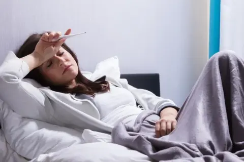Kobieta z gorączką mierzy temperaturę, marząc o ulgę, którą może przynieść Biseptol 960.