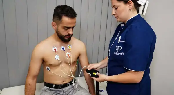 Pacjent z elektrodami EKG na klatce piersiowej, pielęgniarka podłącza urządzenie. To badanie, które odpowiada na pytanie: holter co to jest.