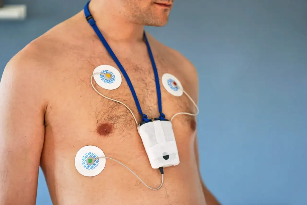 Mężczyzna z przyklejonymi elektrodami EKG i urządzeniem na szyi. To jest holter, który monitoruje pracę serca.