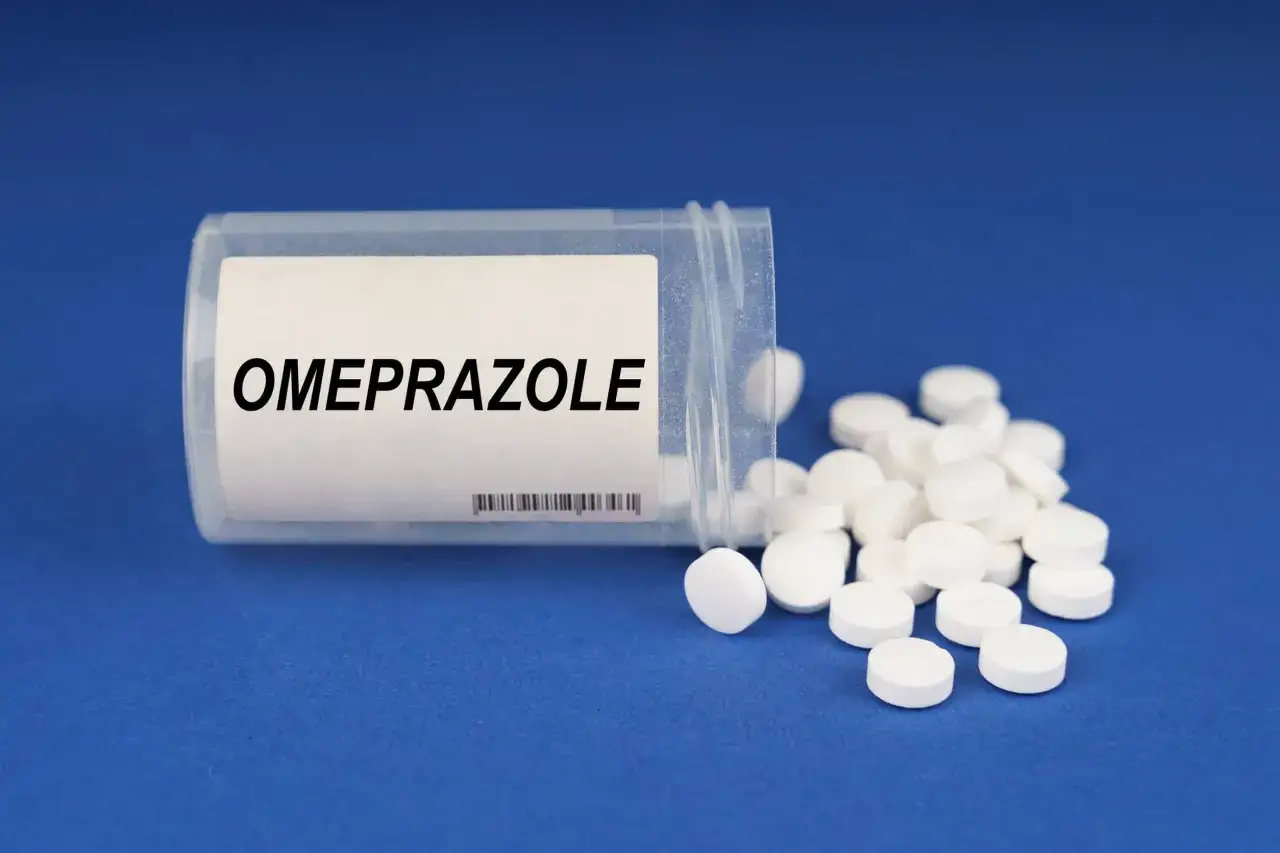 Pojemnik z napisem OMEPRAZOLE, z którego wysypały się białe tabletki. Lek ten często stosowany jest w leczeniu dolegliwości żołądkowych, w tym tych związanych z helicid.