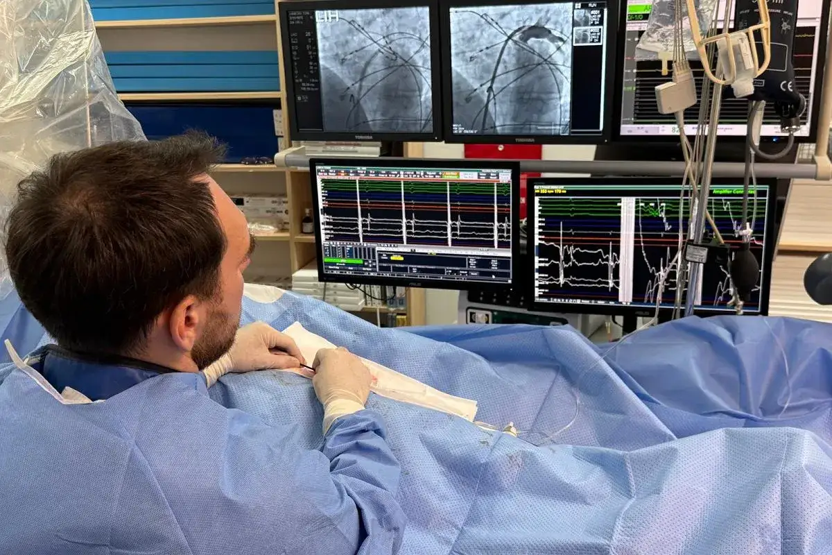 Lekarz w rękawiczkach pracuje przy monitorach pokazujących obraz z zabiegu kardiologicznego. Na ekranach widać przebieg zabiegu, dane EKG i inne parametry życiowe, kluczowe dla procedury biosotal.
